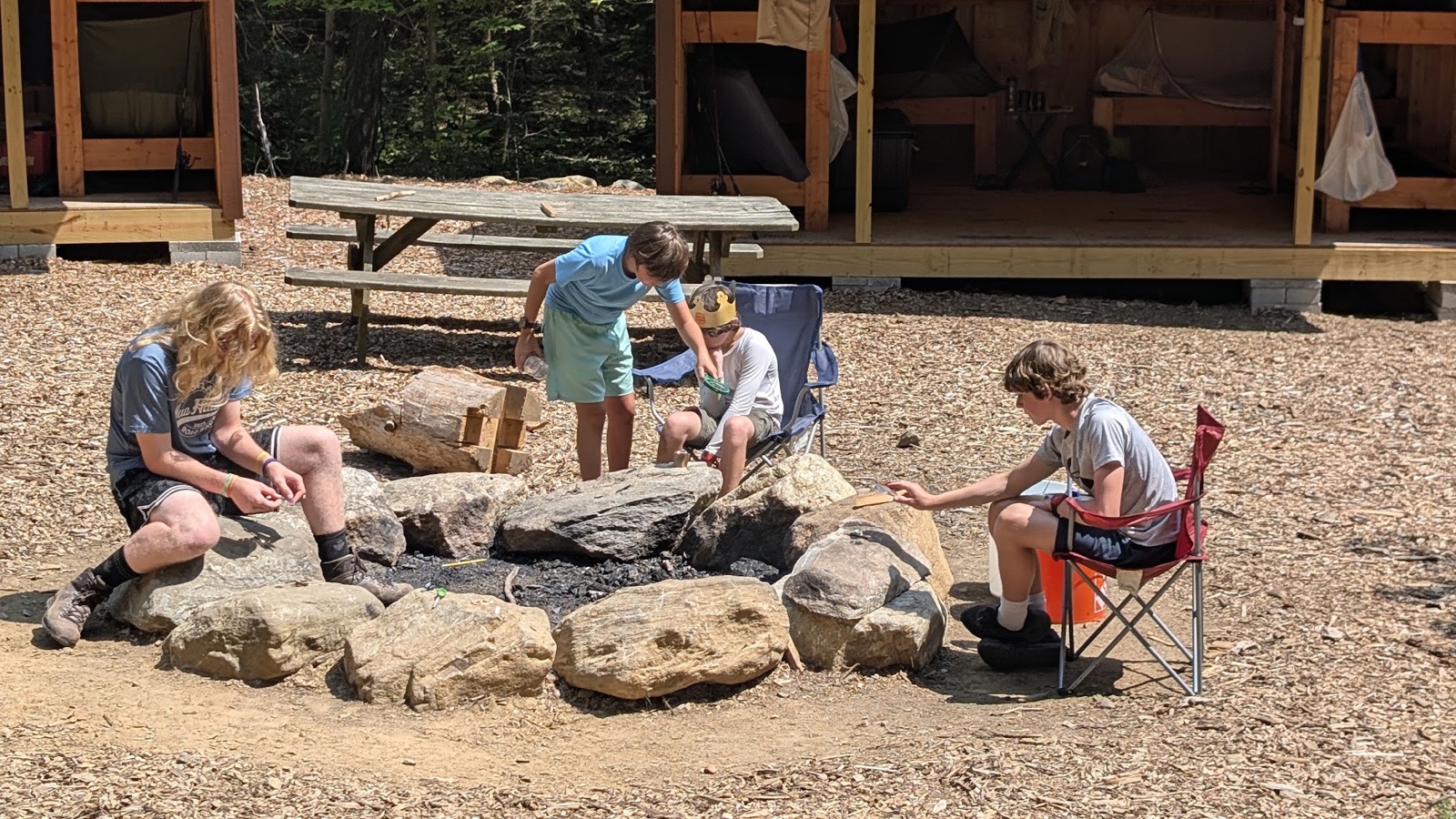 Troop 444 Scouts working around a stone fire ring at a summer camp site.